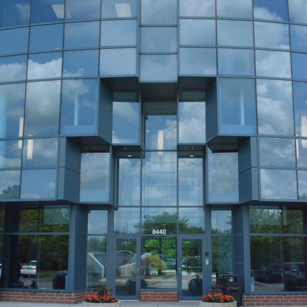 Front view of a curved glass office building with blue-tinted windows and a central glass entrance showing the address 8440 at the door.